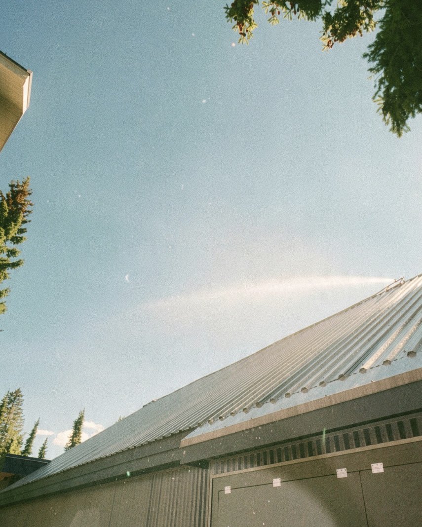 Wildfire sprinkler arcing water across a metal roof under a clear sky