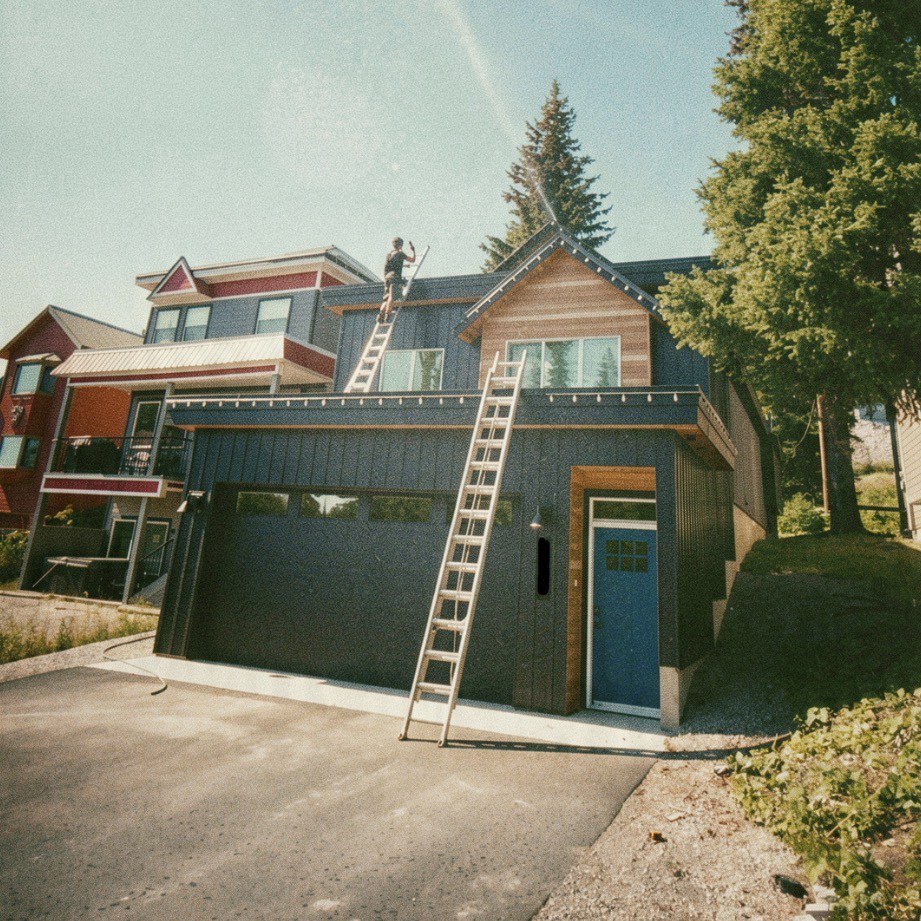 Technician installing a wildfire sprinkler system on the roof of a modern Okanagan home using ladders