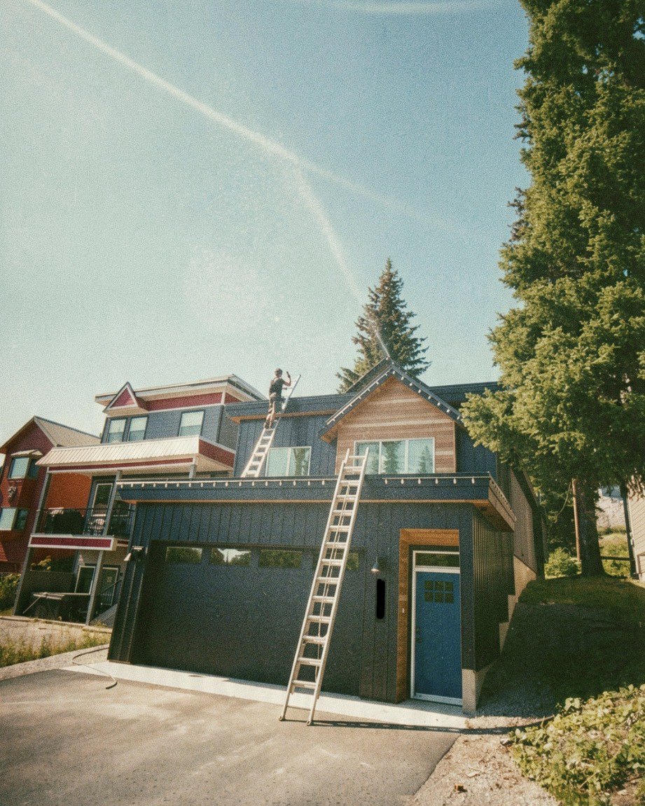 Technician on a ladder installing rooftop wildfire sprinklers on an Okanagan home